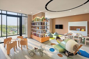 Amplia zona de juegos infantiles con un ventanal grande, una estantería y un televisor.