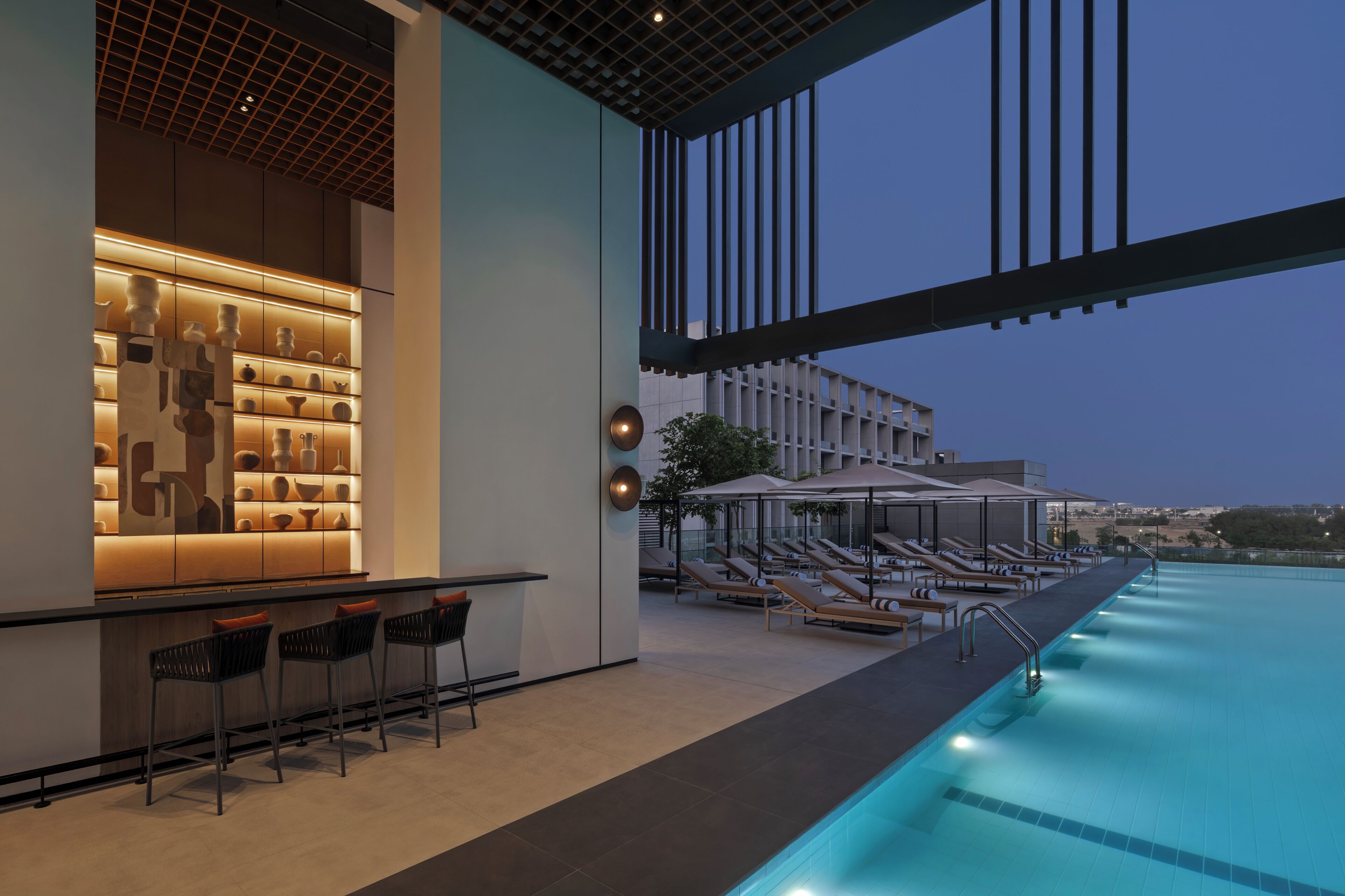 A modern outdoor pool area with lounge chairs and a bar.