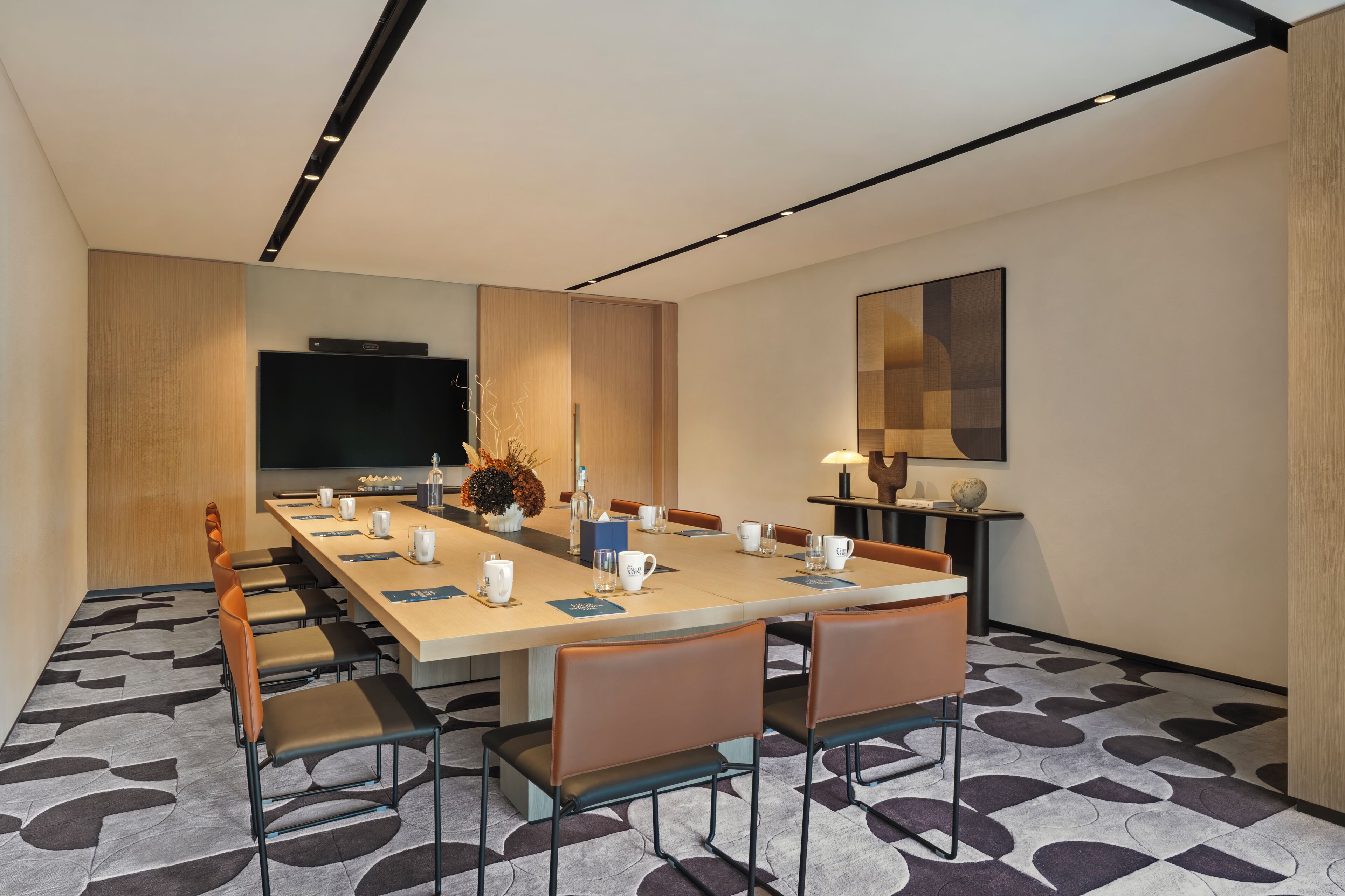 A conference room with a long table, chairs, a flat-screen TV, and a decorative vase.