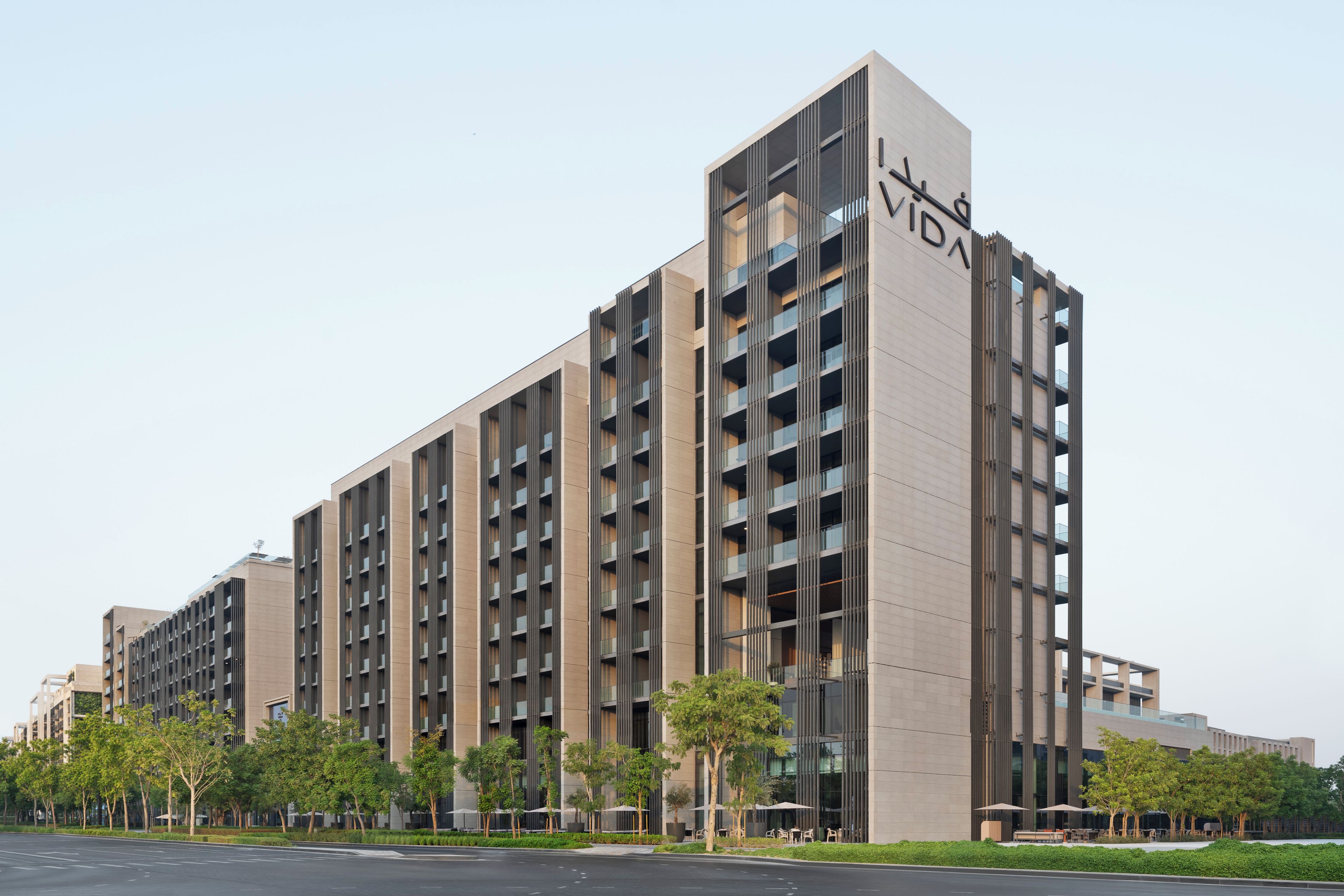 A modern multi-story building with a prominent 'VIDA' sign, featuring a grid of balconies and a flat roofline.