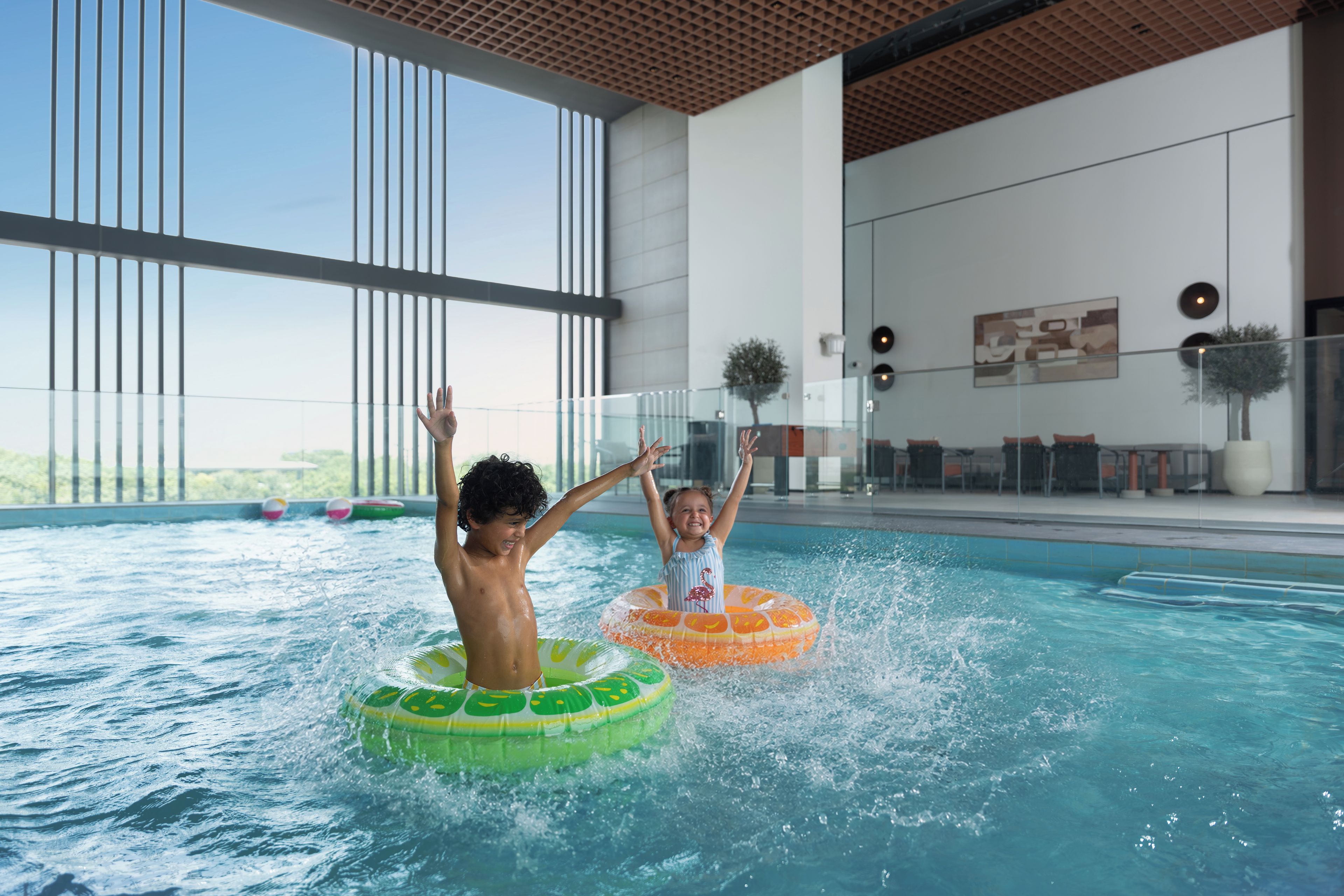 An indoor swimming pool with two children playing on inflatable rings.