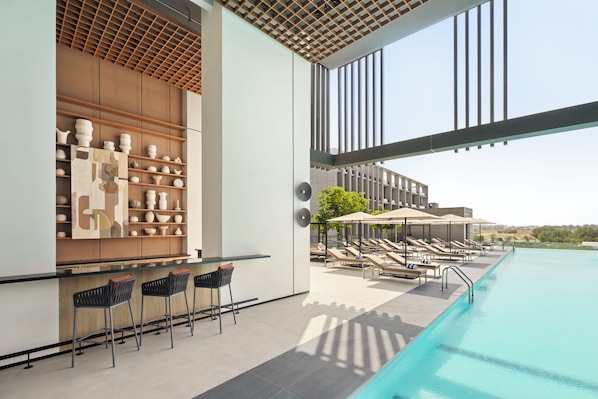 A modern poolside area with lounge chairs and a bar area with shelves of decorative items. - Vida Aljada (Sharjah)