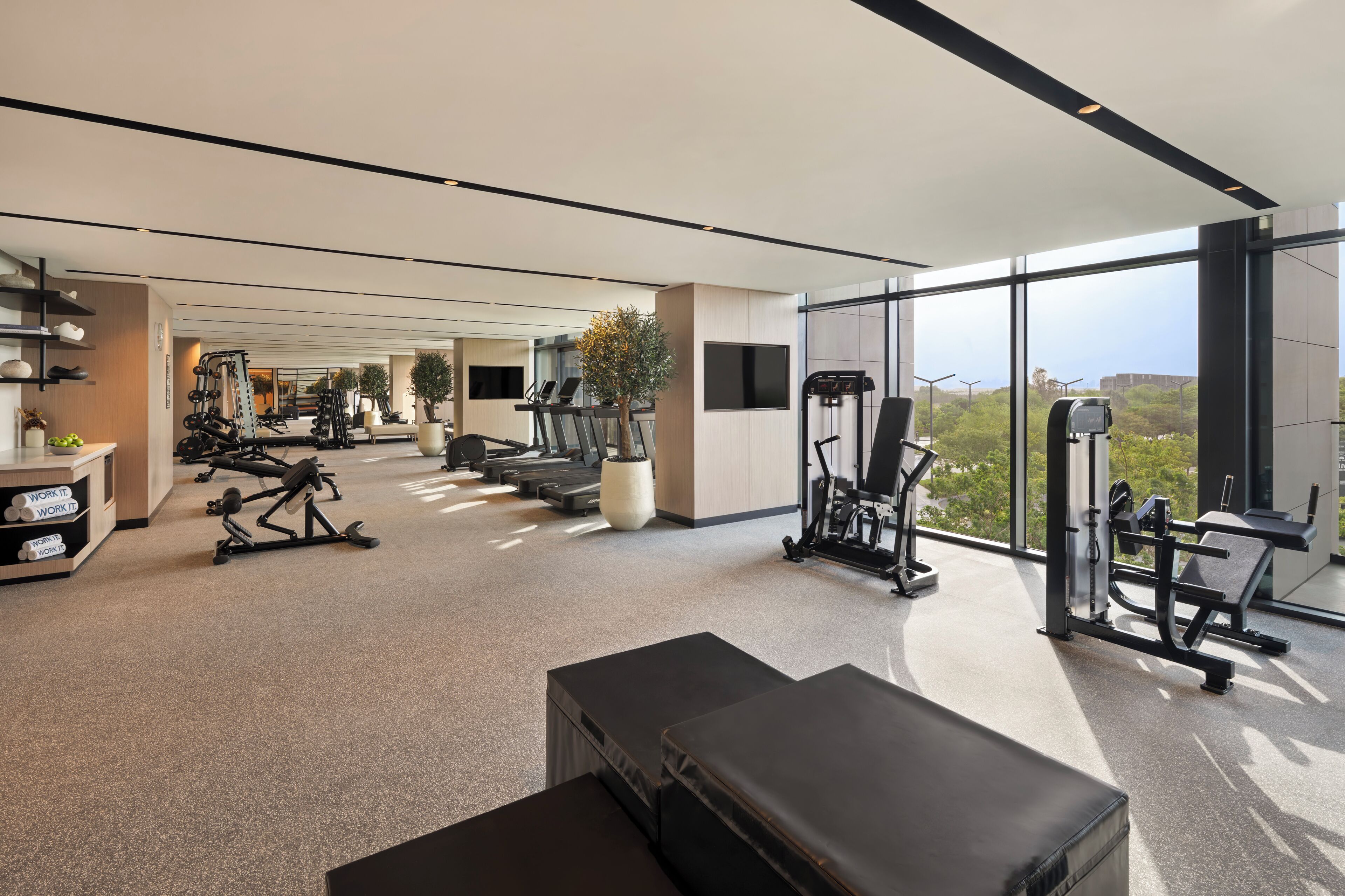 Ein modernes Fitnessstudio mit unterschiedlichen Trainingsgeräten, einer Bank und einem großen Fenster mit Blick ins Freie.