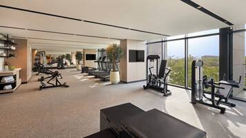 Ein modernes Fitnessstudio mit unterschiedlichen Trainingsgeräten, einer Bank und einem großen Fenster mit Blick ins Freie.