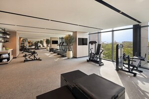 Un gimnasio moderno con diversos equipos de ejercicio, una banca y un amplio ventanal con vistas al exterior.