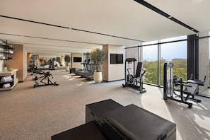 A modern gym with various exercise equipment, a bench, and a large window offering a view of the outdoors. - Vida Aljada (Sharjah)