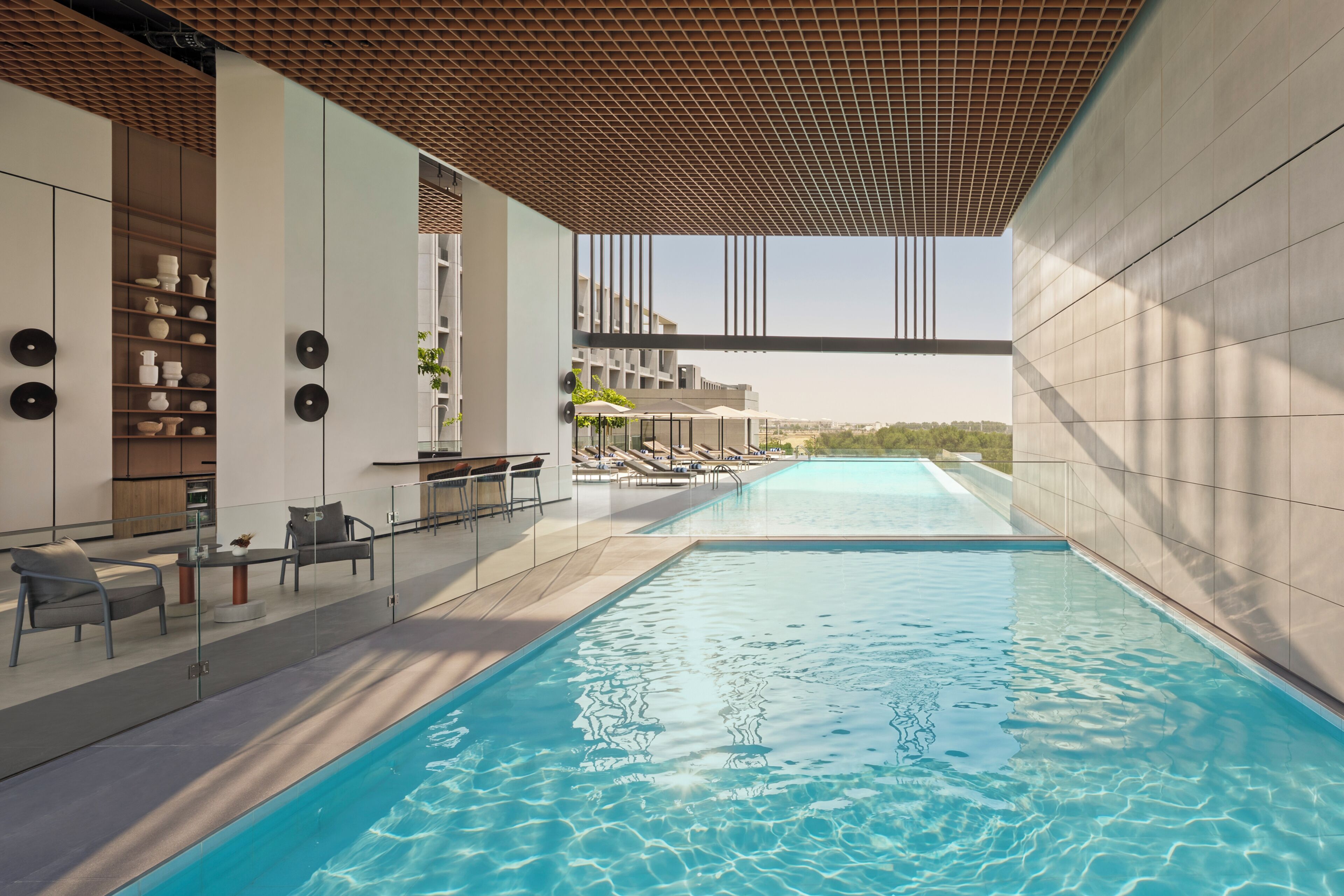 A modern indoor swimming pool with lounge chairs and a glass railing.