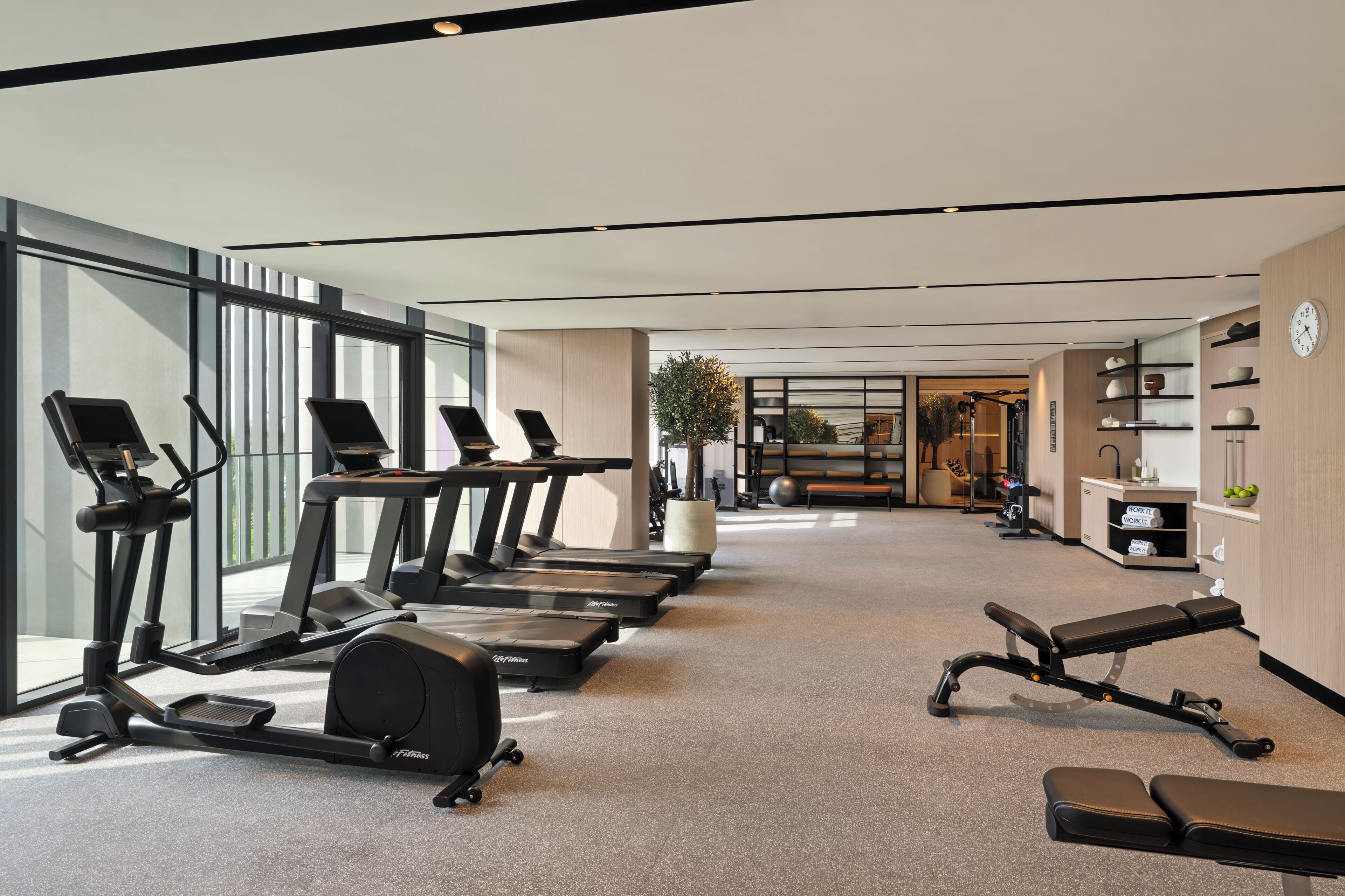 A modern gym with treadmills, a rowing machine, and a bench.