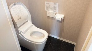 Uma casa de banho moderna com uma sanita branca, um dispensador de toalhas de papel e um manual de instruções fixado na parede.