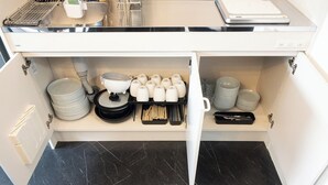 Cozinha com bancada branca, painel de fundo preto e chão em mosaico preto. Há diversos utensílios e louças de cozinha organizados na bancada.
