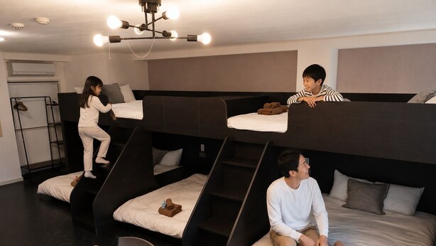 Quarto com beliche, mesa, cadeiras, escada e luminária no teto.
