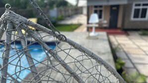 A close-up of a woven rope fence with a chain link structure, leading to a swimming pool area.