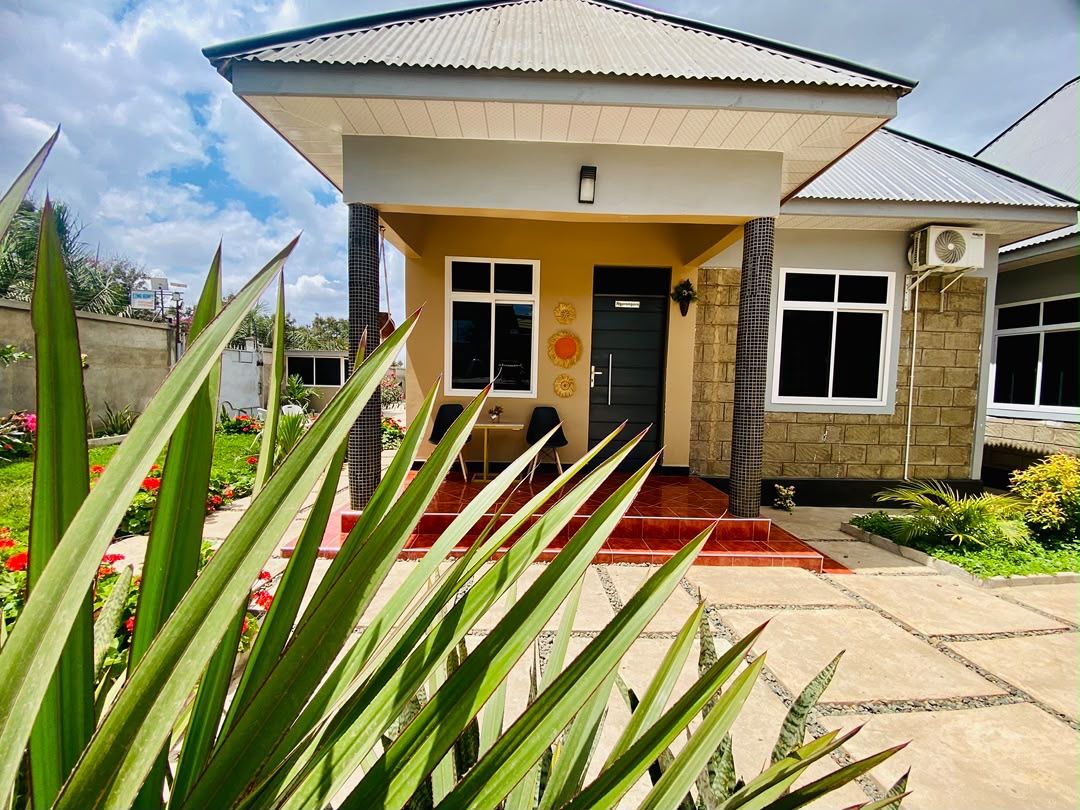 A house with a tiled entrance, a small porch, and a garden with tropical plants.