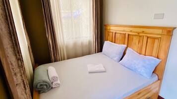 A single-bed room with a wooden headboard, a red rug, and a window with curtains.