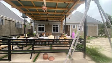 Un área de comedor al aire libre con techo cubierto, mesas, sillas y un columpio de cuerda.