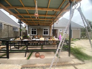 Een terras buiten met een overdekt dak, tafels, stoelen en een touwschommel.