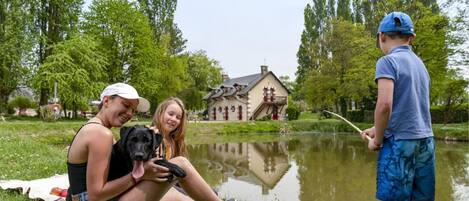 A group of people sitting by a pond with a house in the background.