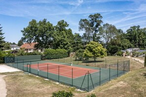 Tennisbane omgivet af træer og huse.