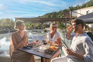 A dining table with plates of food and drinks, overlooking a pool and a mountainous landscape.