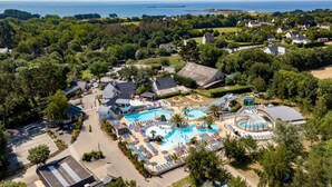Luftaufnahme eines Resorts mit großem Schwimmbad, Wasserrutsche und Strandabschnitt.