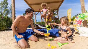 Eine Szene vom Strand mit spielenden Menschen, einem Strandsonnenschirm und einer Flagge.