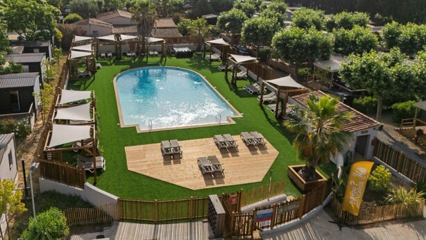 Ein Swimmingpool, umgeben von Liegestühlen und Sonnenschirmen, mit einer Holzterrasse und einem eingezäunten Bereich.