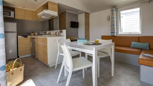 Eine kompakte Küche mit Mikrowelle, Herd und Spüle. Ein Esstisch mit Stühlen und eine Couch mit Kissen sind vorhanden. Ein Fernseher ist an der Wand montiert.