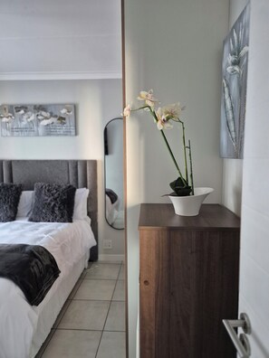 Un dormitorio moderno con una cama, una mesita de noche de madera y un florero con flores.
