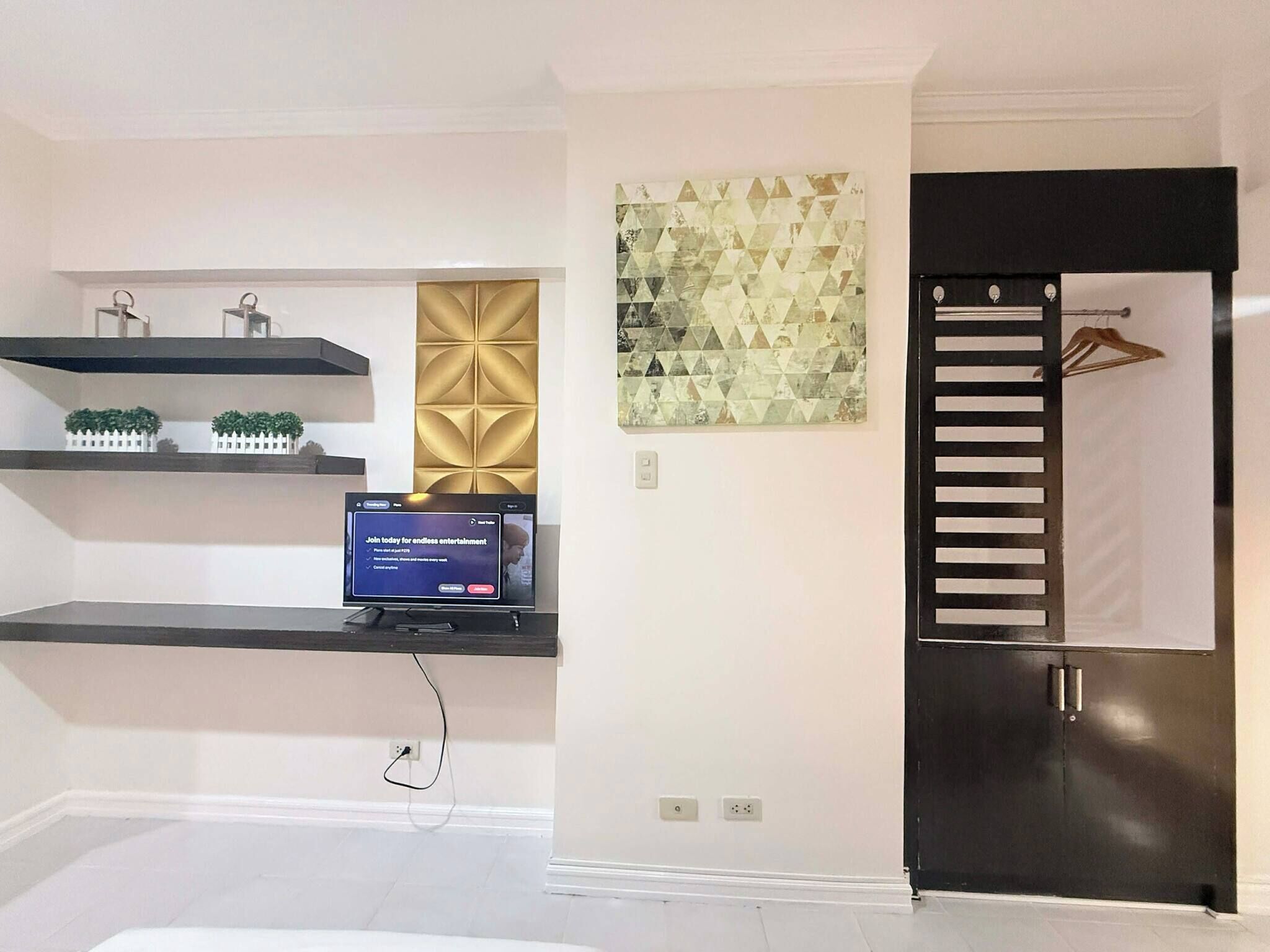 A modern living room with a flat-screen TV on a black stand, a decorative wall panel, and a black wardrobe with a hanging rod.