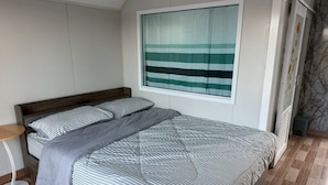 Een slaapkamer met een bed, een raam met een gestreept gordijn, een klein nachtkastje en een wand met een marmerlook.