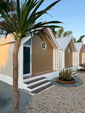 A row of modern, single-story cabins with a minimalist design, featuring a wooden facade and a small circular window on each unit.