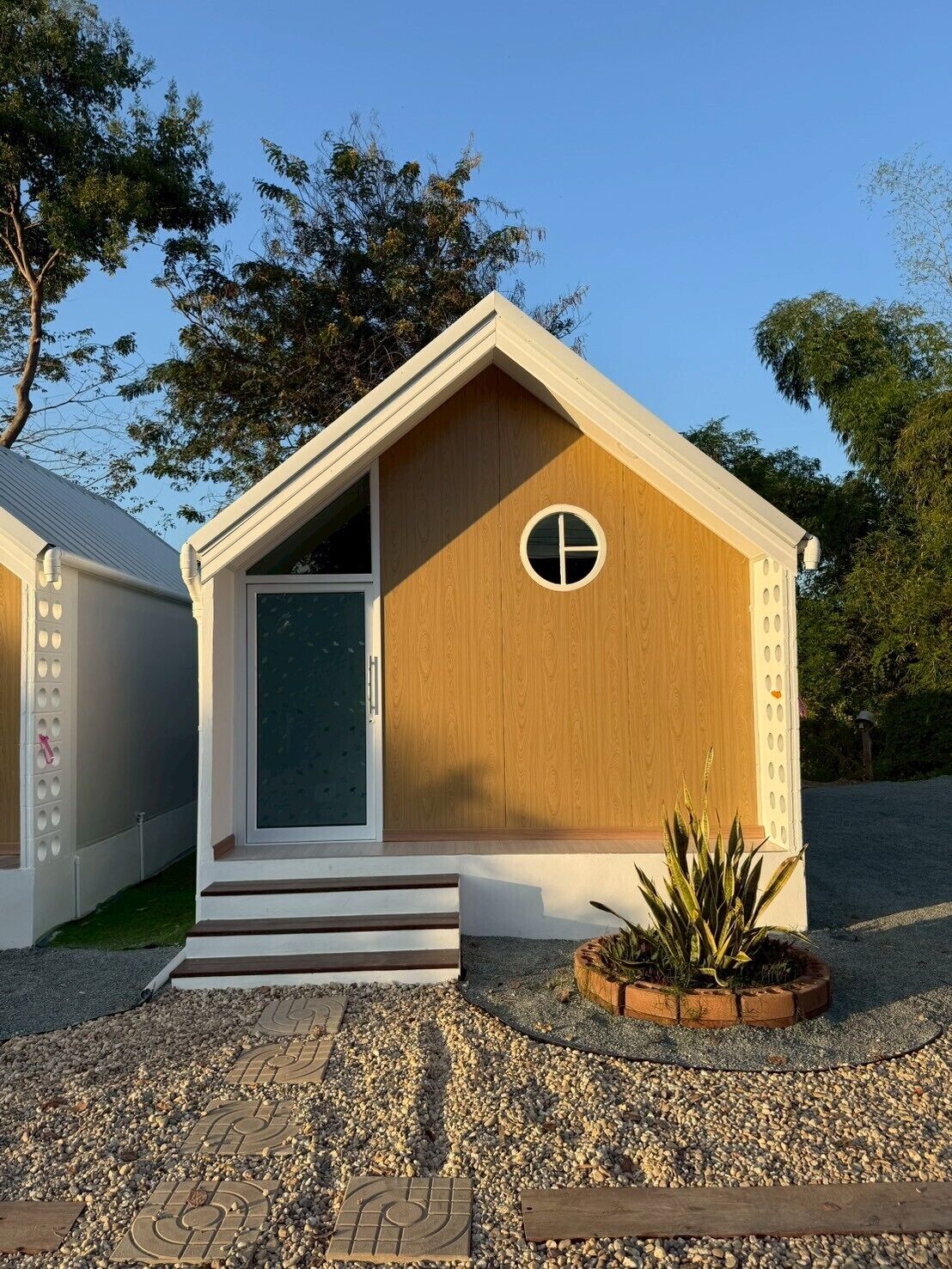 Un pequeño edificio de madera con techo triangular, una puerta y un ventanal circular.
