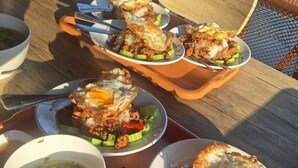 Een dienblad met eten, waaronder gebakken eieren, vlees en groenten, plus kommen soep en dipsauzen.