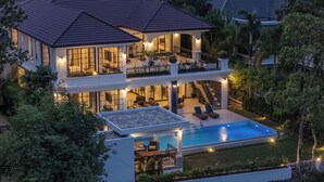 Une maison à deux étages avec une piscine, un espace salon extérieur et un balcon bien éclairé.