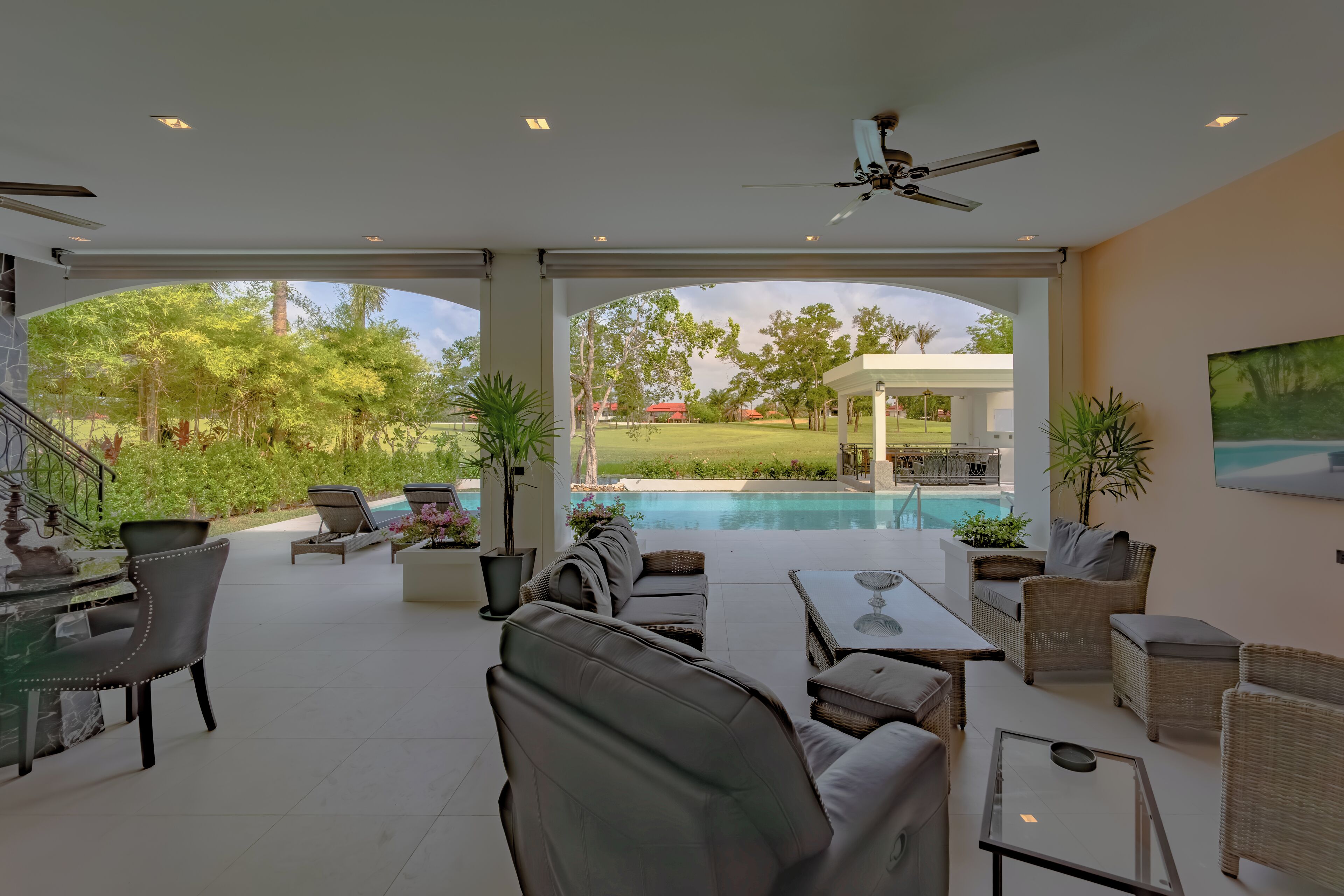 A spacious outdoor area with a pool, comfortable seating, and a ceiling fan.