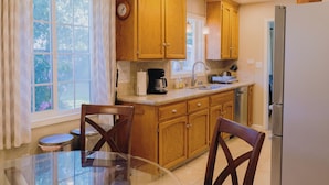 A kitchen with wooden cabinets, a refrigerator, a coffee maker, and a window with curtains.