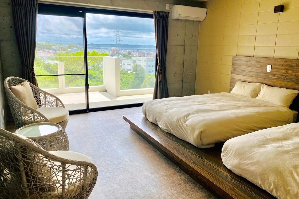 Une chambre d’hôtel avec un lit, une chaise, une petite table et une vue sur la ville grâce à de grandes fenêtres.
