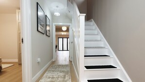 Eine Treppe mit weißen Stufen und schwarzen Wangen, ein Flur mit einem gemusterten Teppich und gerahmten Bildern an der Wand.