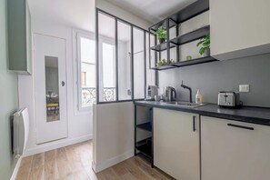 A modern kitchen with white cabinets, black countertops, and a built-in shelf with plants. - Charming 1 Bedroom Ideally Located in Paris (Paris)