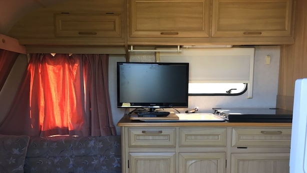 A compact RV kitchen with a flat-screen TV, wooden cabinets, and a dining area with a table and bench. - Heart Land Hills In Noto 37 Trailer House Sho (Nanao)
