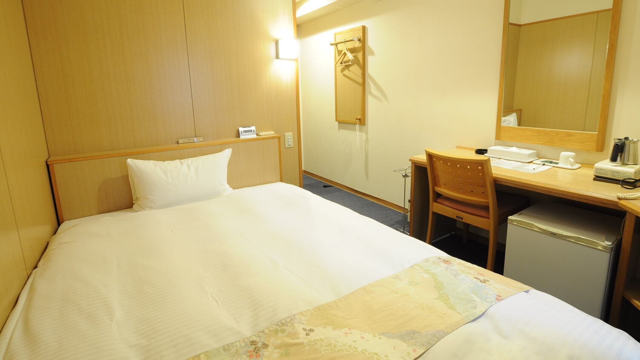 Une chambre d’hôtel équipée d’un lit, d’un bureau, d’une chaise, d’un miroir et d’un petit réfrigérateur.