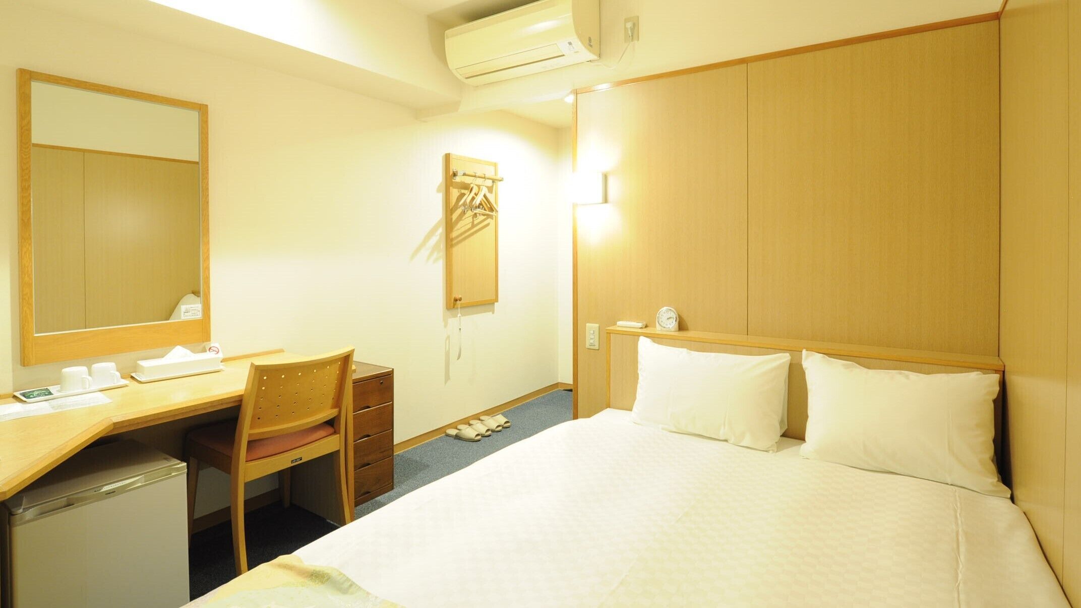 Une chambre d’hôtel équipée d’un lit, d’un bureau, d’une chaise, d’un miroir, d’une armoire et d’un appareil de climatisation.