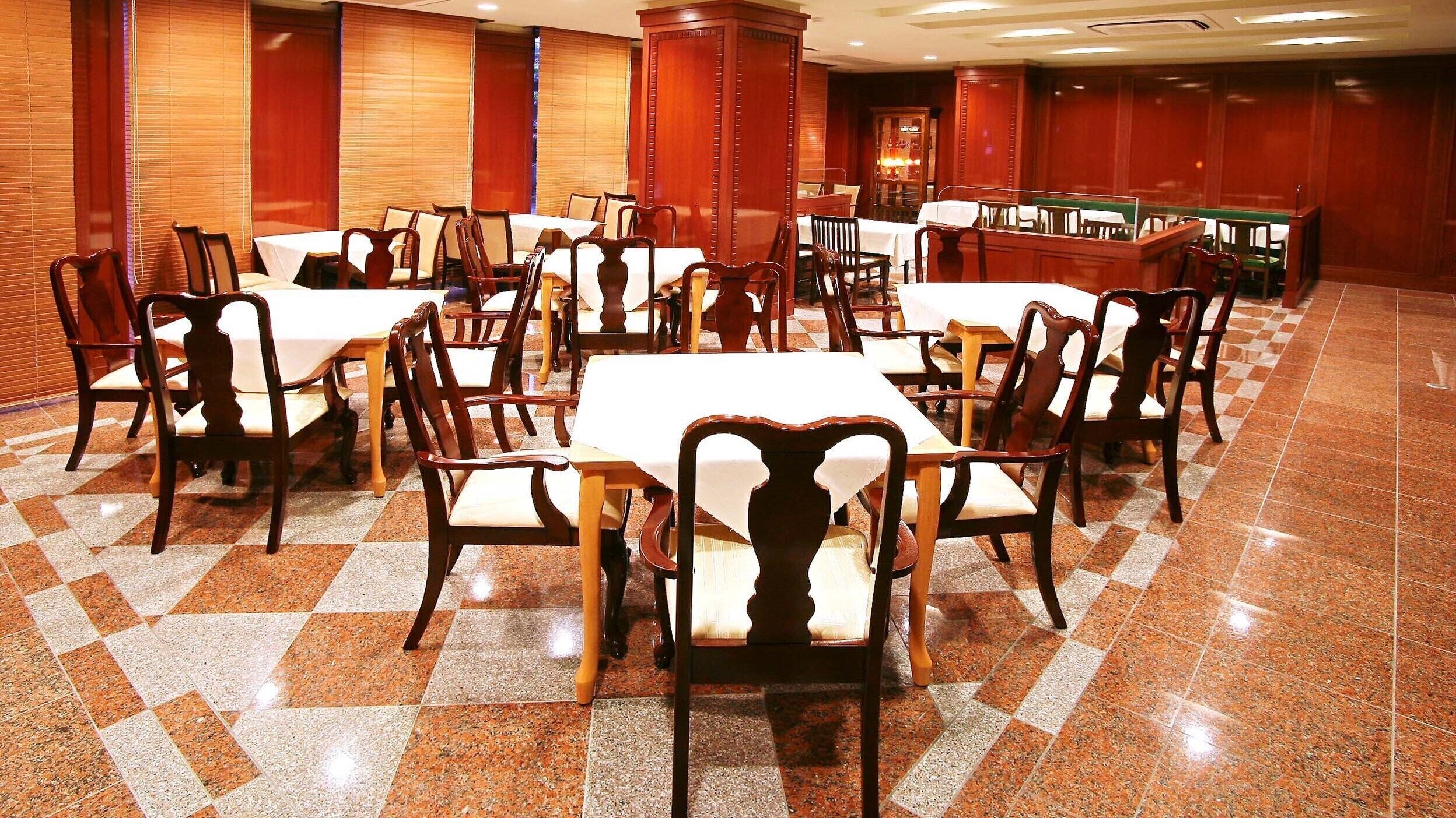 A spacious dining area with multiple tables and chairs, a checkered floor, and wooden paneling on the walls.