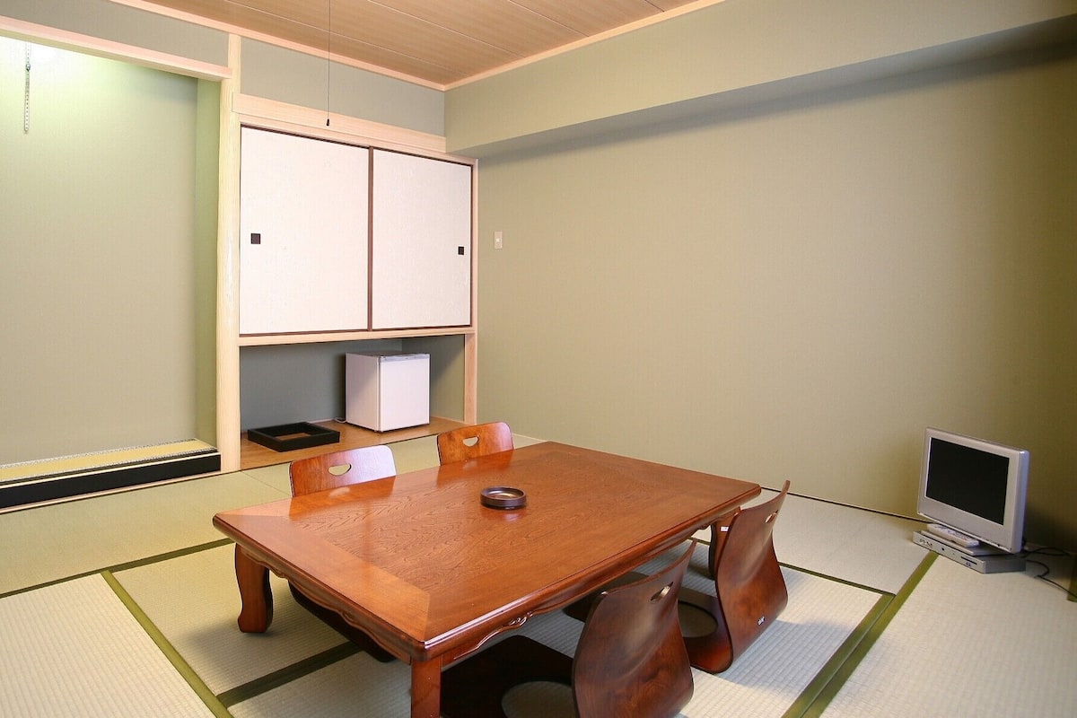 A small room with a wooden table and chairs, a television, and a refrigerator.