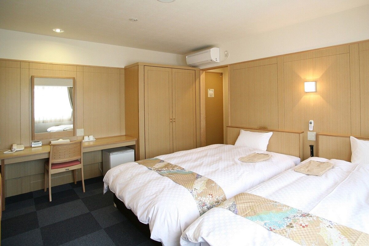A hotel room with a bed, a desk, a chair, a mirror, and a wardrobe.
