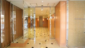 Un hall d’hôtel avec une entrée dotée d’une porte en verre, un sol carrelé et un mur orné d’un motif en quadrillage.