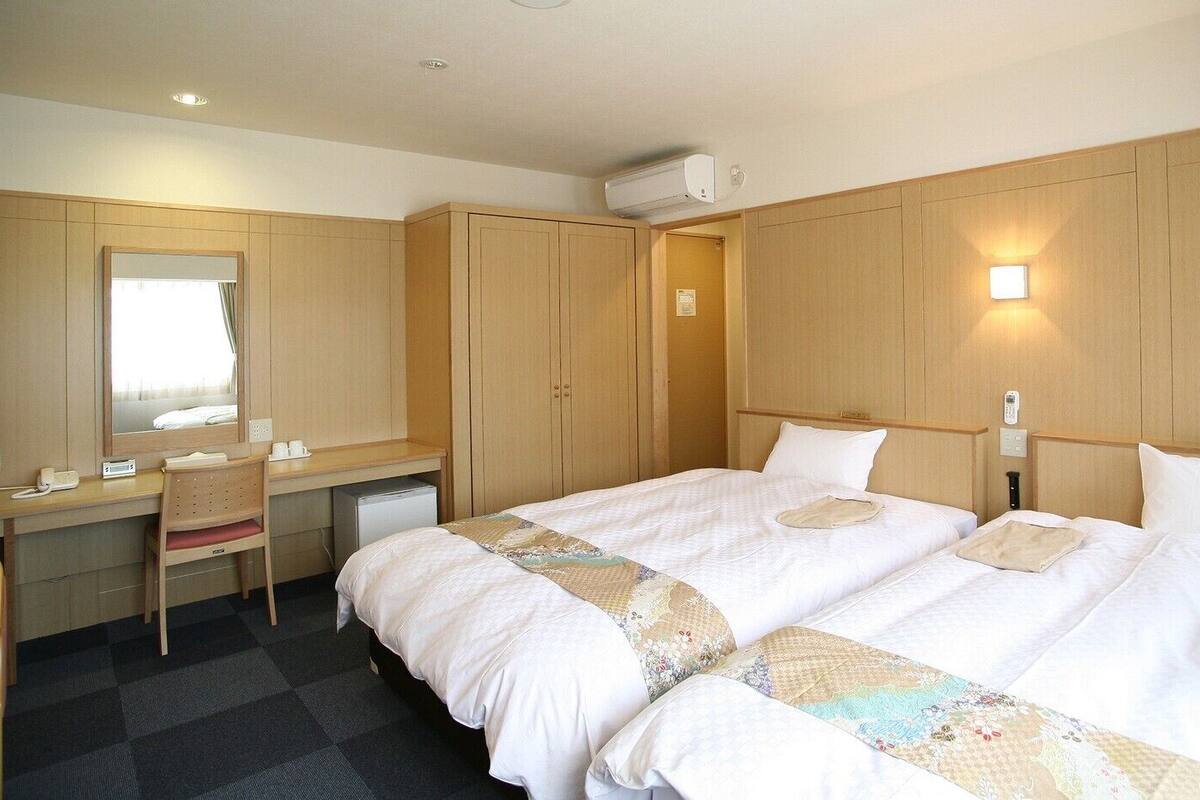A hotel room with a bed, a desk, a chair, a mirror, and a wardrobe.