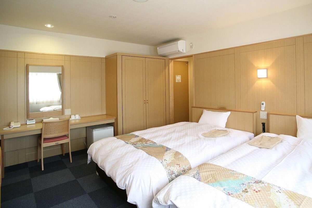 Hotellihuone, jossa on sänky, työpöytä, tuoli, peili ja vaatekaappi.