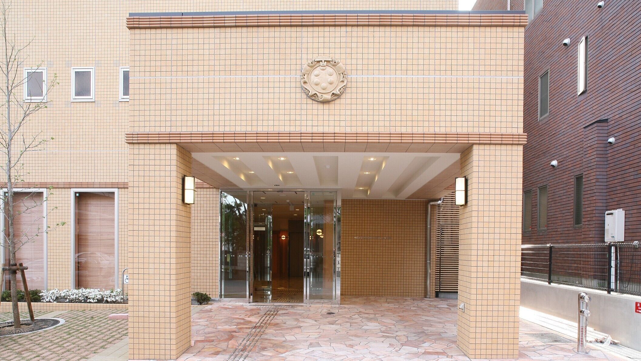 Fachada de hotel con azulejos, puerta de cristal y un pequeño espacio exterior con un hidrante.