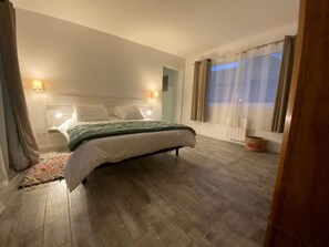 Ett sovrum med en säng, sänglampor, ett fönster med gardiner och ett trägolv.